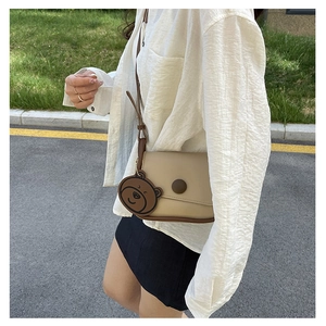 Détail du sac beige avec bordure brune, boucle ronde et charmant pendentif en forme d'ours