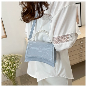 Close-up of sky blue textured handbag featuring a unique pearl handle and curved base