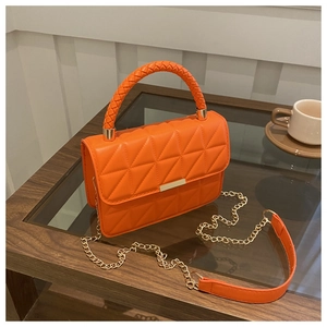 Close-up of orange quilted crossbody bag with gold hardware on a modern wooden coffee table