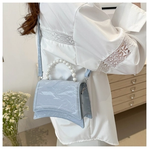 Macro detail of a light blue pearlescent bag featuring a unique curved base and pearl handle
