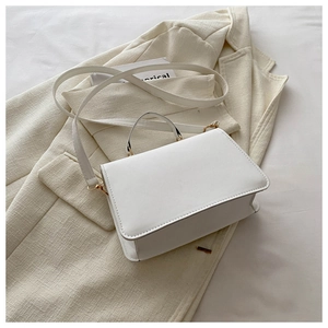 Close-up of white leather handbag texture with gold hardware on a beige blazer