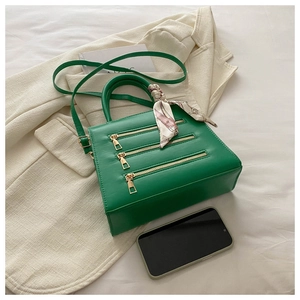 Detail of green leather handbag with gold zippers, decorative scarf and phone for scale