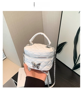 Detailed view of white quilted crossbody bag with silver butterfly charm and chain strap