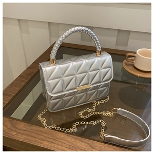Silver quilted handbag with woven handle and gold chain strap detail on wooden table