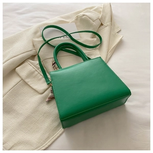 Close-up of emerald green square handbag with decorative silk scarf and sleek leather texture