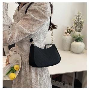 Detail of black V-quilted underarm bag with gold chain strap on a floral dress background