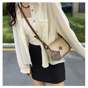 Sac bandoulière beige avec bordure marron et breloque ours porté par un mannequin