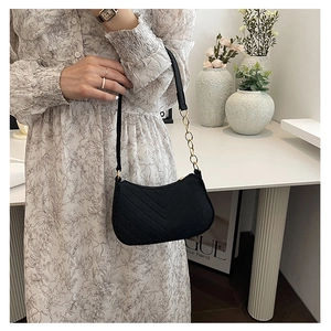 Model wearing a black V-quilted shoulder bag with gold chain strap in a bright interior