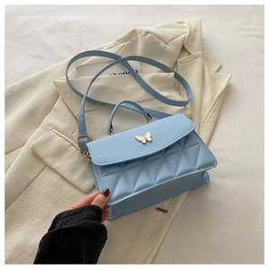 Detail view of light blue quilted square bag with butterfly clasp on white blazer