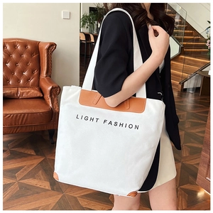 Detail of large canvas tote bag with brown leather trim carried by a model in a cafe