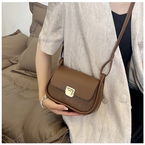 Detail of a brown quilted crossbody bag with a gold square buckle shown on a shoulder
