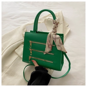Detail of green leather handbag with decorative gold zippers and silk scarf handle
