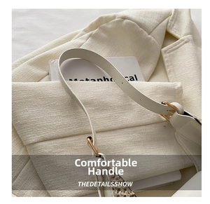 Detail view of the thin cream leather strap and metal buckle on this crescent bag