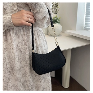 Detail of black faux suede underarm bag featuring V-shaped quilting and gold chain strap