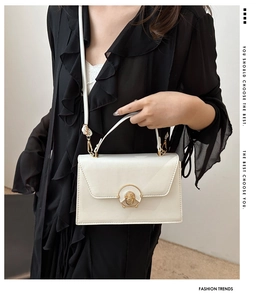 Detail view of cream white flap bag featuring a golden circular clasp and strap