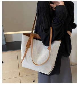 Minimalist canvas tote bag with brown leather handles worn over the shoulder for daily commute