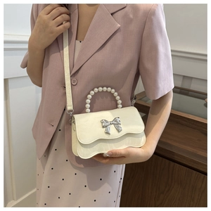 Detail of white bow bag with pearl handle and wave flap, worn with a pink suit