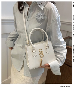 Elegant white leather crossbody bag with gold logo and tassel on a stylish model