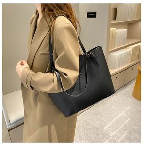 Close-up of a large black matte leather tote bag with gold hardware worn by a model