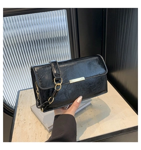 Detail of black oil-wax leather shoulder bag with golden metal trim and chain strap