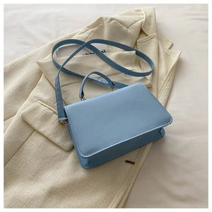 Detailed view of light blue crossbody bag on a beige blazer with gold hardware