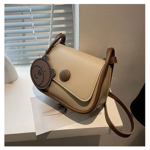 Détail du sac à selle vintage beige avec bordure marron et breloque ours mignonne