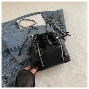 Detailed shot of black bucket backpack with silver zippers and chain strap on denim