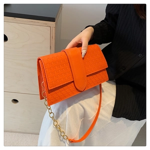 Detail of orange handbag featuring woven texture and gold chain strap in hand
