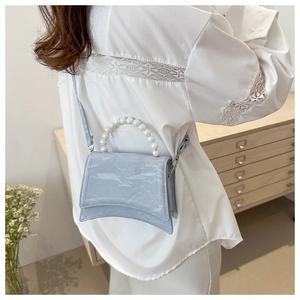Detail of light blue shoulder bag with pearl handle and curved base on lace shirt
