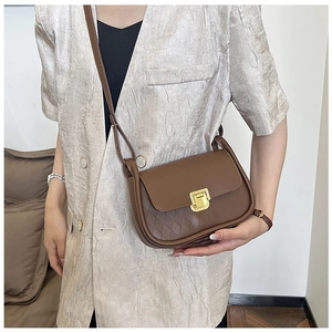Close-up of brown leather crossbody bag with quilted pattern and gold square metal clasp