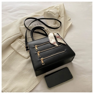 Close-up of black leather square bag with triple gold zippers and silk scarf handle