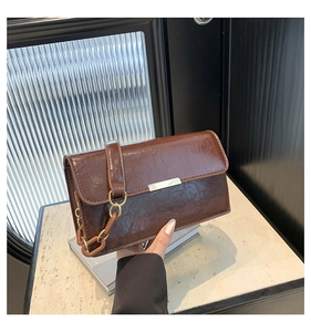 Detail of dark brown crinkled leather handbag with gold metal bar and chain strap detail