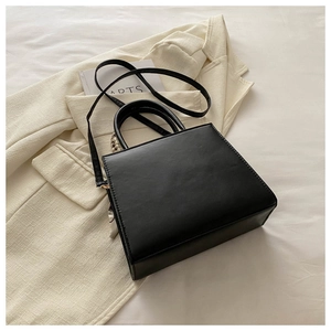 Detail view of a black minimalist leather handbag with silk scarf and top handles