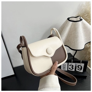 Detail of minimalist cream and brown crossbody bag with decorative round buckle on desk