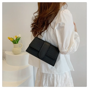 Detail of black geometric embossed shoulder bag with gold chain on model in white dress