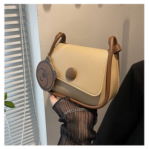 Détail d'un sac besace beige et marron avec pendentif ours et fermoir métallique