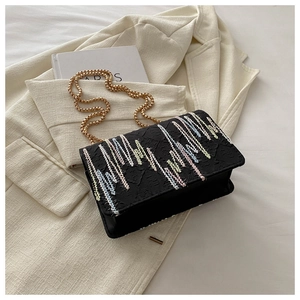 Detail view of black crossbody bag with colorful wavy embroidery and golden bead chain