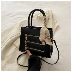 Detail of black handbag with decorative zippers, silk scarf handle, and gold hardware