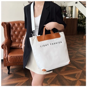 Detail of white canvas tote bag with brown leather handles and Light Fashion lettering