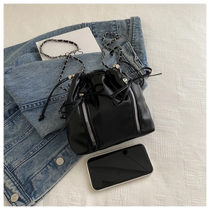 Close-up of black drawstring bucket bag featuring silver zippers and chain strap