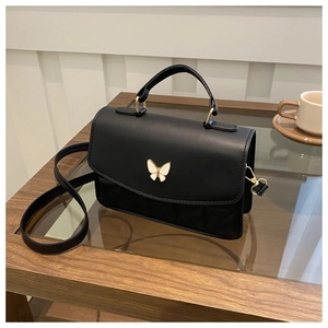 Detail of matte black quilted crossbody bag with white butterfly metal buckle on table