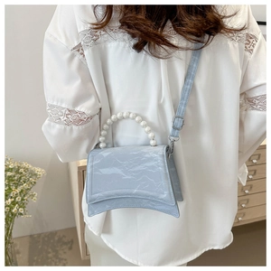 Detail of light blue crossbody bag with pearl handle and marble texture on white lace dress