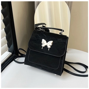 Detail of black textured square bag with silver butterfly emblem and top handle