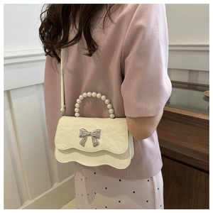 Detail of white crossbody bag with pearl handle, wavy edge, and silver bow accent