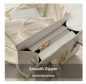 Detailed close-up of smooth gold metal zipper and logo on white leather handbag