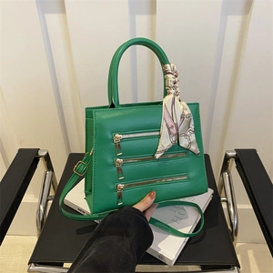 Detail of green leather handbag with decorative gold zippers and vintage silk scarf wrap