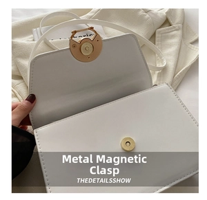 Detail shot of a matte gold magnetic clasp and fine stitching on a white leather handbag