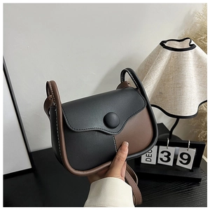 Close-up of black and brown leather crossbody bag with circular buckle and white stitching