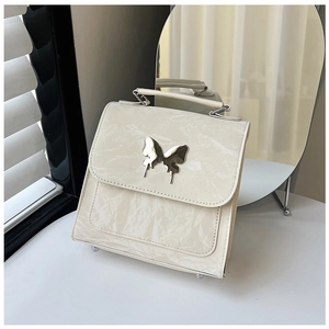 Detail of cream white textured handbag featuring a silver butterfly metallic ornament