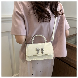 Detail of white leather shoulder bag with pearl handle and silver bow accent on a model
